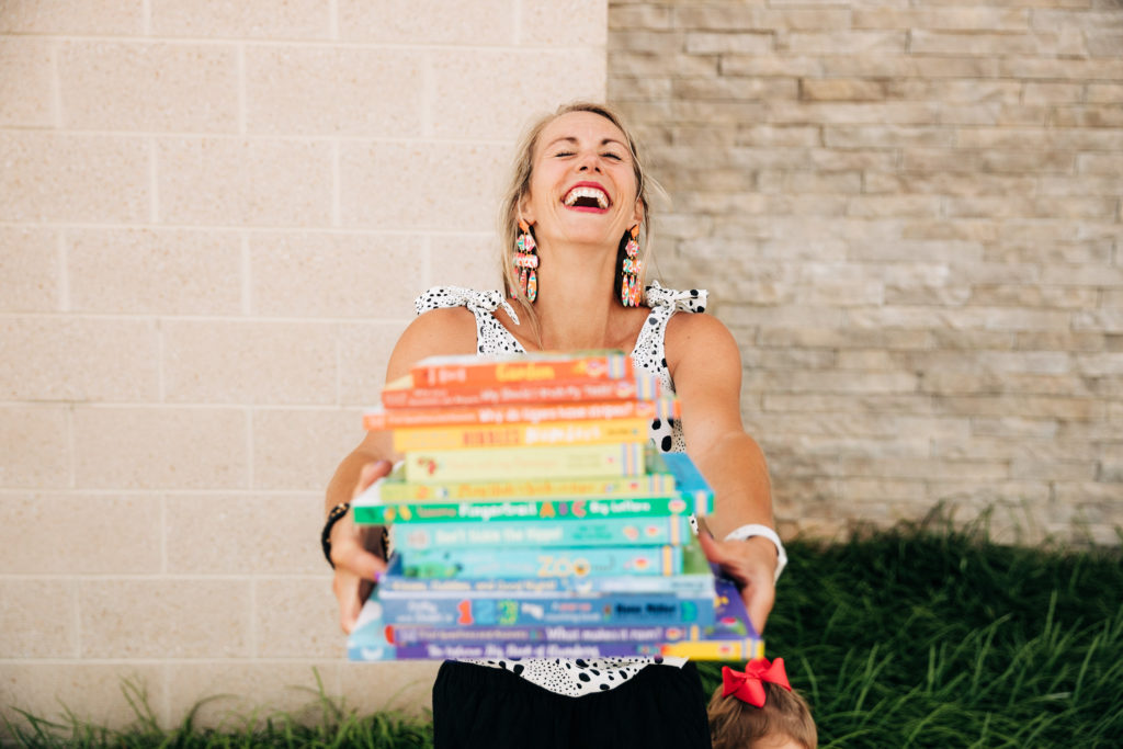 Brand photo of a woman laughing holding a stack of books in rainbow order..