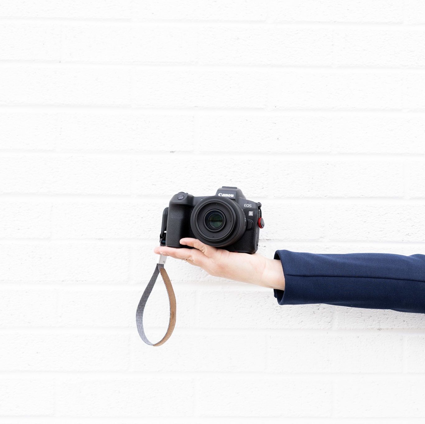 BH Brand Co. Brand Photographer holding a camera with a straight arm along a white brick wall.